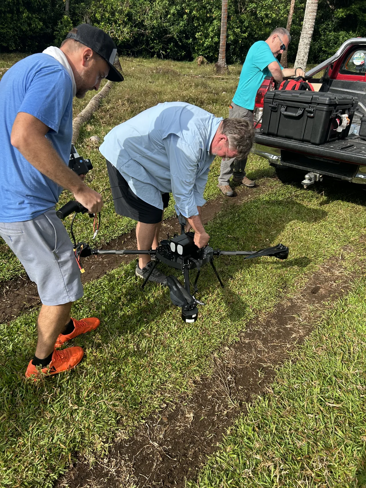 Crew preparing a Patriot quadcopter and its batteries beside a pickup truck and equipment cases